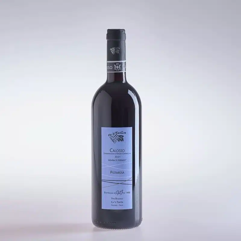 Fotoaufnahme zeigt Rotwein Piotarùsa Calosso von Winzer Ca 'd Tantin. Geschmack Der Wein beeindruckt mit einem gehaltvollen und zugleich raffinierten Geschmacksprofil, das sofort seine Vielseitigkeit und Klasse offenbart. Im ersten Moment zeigt er sich auf der Zunge mit einer ausgewogenen Balance und einer samtigen Textur, die angenehm ausgewogen und harmonisch wirkt. Der elegante Eindruck setzt sich fort im Zusammenspiel zarter Fruchtaromen mit einem Hauch reifer Beeren. Diese Fruchtnoten sind subtil, unterstrichen von einer feinen Würze, die dem Wein eine interessante Tiefe verleiht. Gerade diese Würze offenbart sich durch Nuancen, die an pfeffrige und leicht vegetale Akzente erinnern, was dem Wein eine dynamische und lebendige Struktur verleiht. Am Gaumen präsentiert sich der Wein klar und trocken, wobei diese Trockenheit den intensiven Geschmacksnuancen Raum zur Entfaltung gibt. Der Abgang ist lange und hinterlässt ein sauberes, angenehmes Finish, das noch einmal die Ausgewogenheit und die feine Textur unterstreicht. Ein besonderes Merkmal dieses Weins ist seine Fähigkeit zur Reifung. Diese Lagerfähigkeit ermöglicht es, dass sich die Aromen mit der Zeit weiterentwickeln und der Wein an Komplexität und Tiefe gewinnt. Die sorgfältig ausgewogene Struktur und die präsenten, aber gut eingebundenen Tannine machen ihn zu einem hervorragenden Kandidaten für eine längerfristige Lagerung, in der er sein volles Potenzial entfalten kann