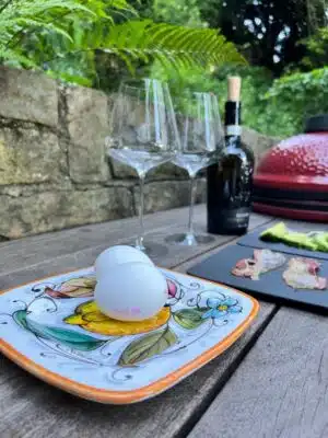 Fotoaufnahme Zeigt ei Kamado Joe Grill mit essen und Rotwein in Hintergrund